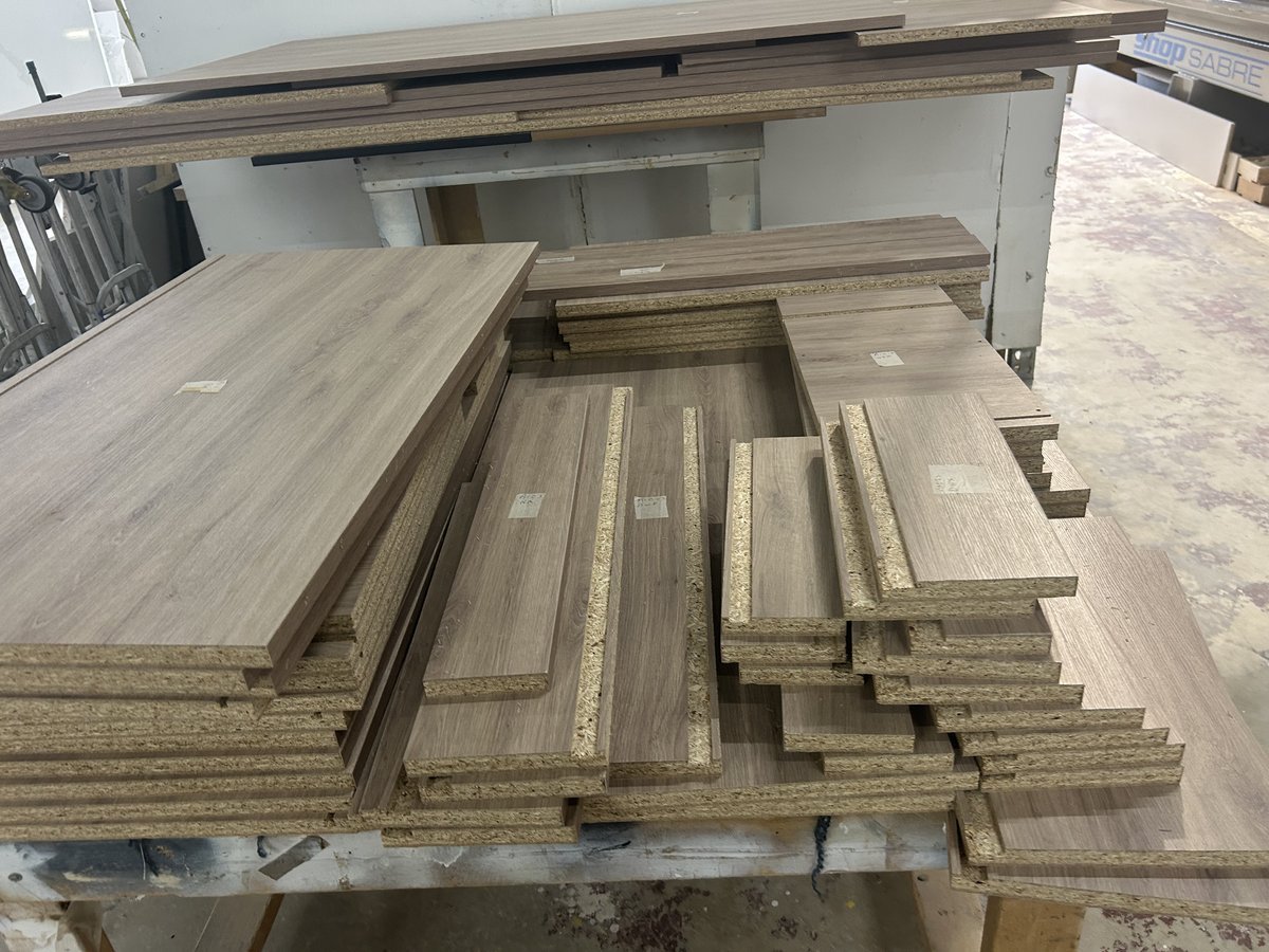 Cabinet parts cut on the CNC and edgebanded, labeled by cabinet, on the bench in the M11 Design Group shop